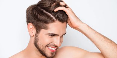 Un hombre sonriente, pasando su mano por el cabello, mostrando una expresión contenta y relajada.