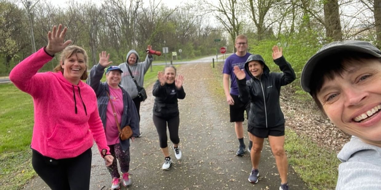 A group of seven people joyfully waving on a forest trail.