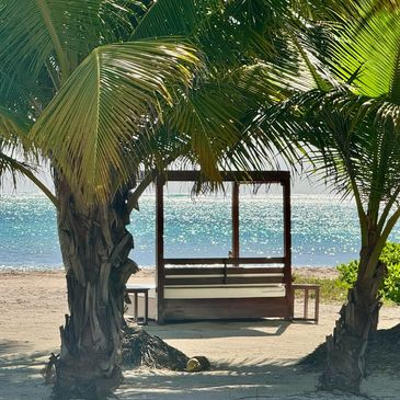 A wooden swing on a beach framed by palm trees.