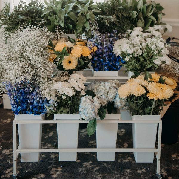 Assorted flowers in white containers on a stand.