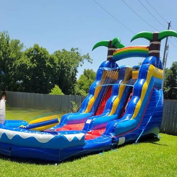 A colorful inflatable water slide with palm trees and rainbow in a backyard.