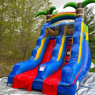 Colorful inflatable slide with palm trees and rainbow design outdoors.