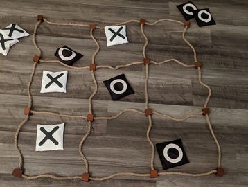 A tic-tac-toe game made with cloth pieces and rope on a wooden floor.