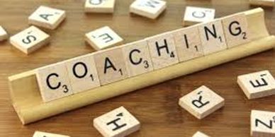 Scrabble tiles spelling out the word 'COACHING' on a wooden rack.