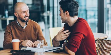 Two men having a friendly conversation at a table with documents and drinks.