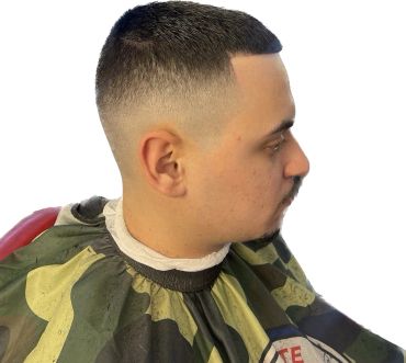 Man with a fresh fade haircut wearing a camouflage barber cape.