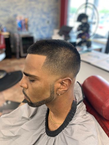 Man with a fresh fade haircut and lined beard sitting in a barber chair.