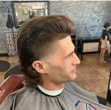 A man with a styled mullet haircut sitting in a barbershop chair.