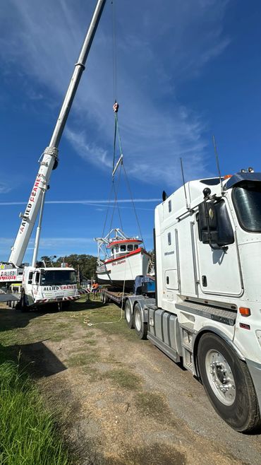 A crane lifts a boat onto a flatbed truck under a clear blue sky.