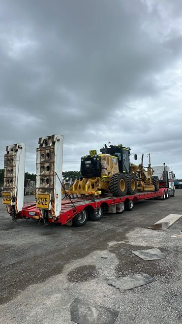 Heavy construction equipment loaded on a red flatbed trailer under a cloudy sky.