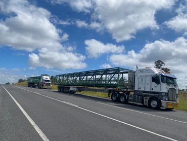 Two large trucks carrying oversized green metal structures parked on the roadside.