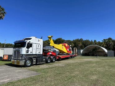 A truck transporting a yellow and red rescue helicopter on a flatbed trailer.