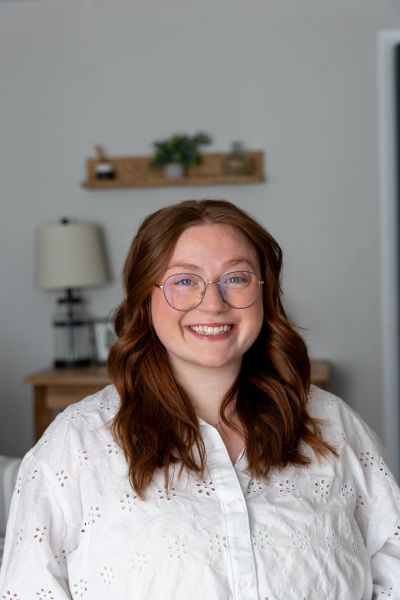Smiling woman with red hair and glasses wearing a white blouse.