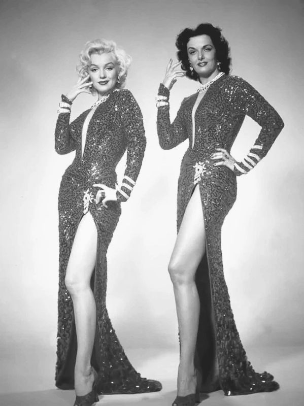 Two women in matching sparkling red gowns with high slits.