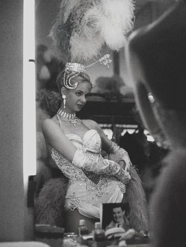 Woman in glamorous showgirl costume adjusting costume in front of mirror.