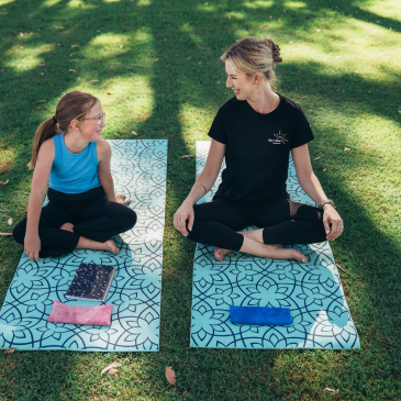 Woman and girl sitting on yoga mats outdoors, smiling.