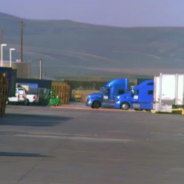 Blue trucks parked in an industrial area with mountains in the background.