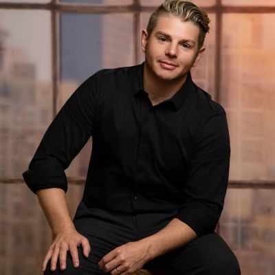 Man in a black shirt sitting and smiling indoors.