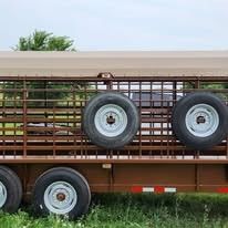 Metal livestock trailer with two spare tires mounted on the side.
