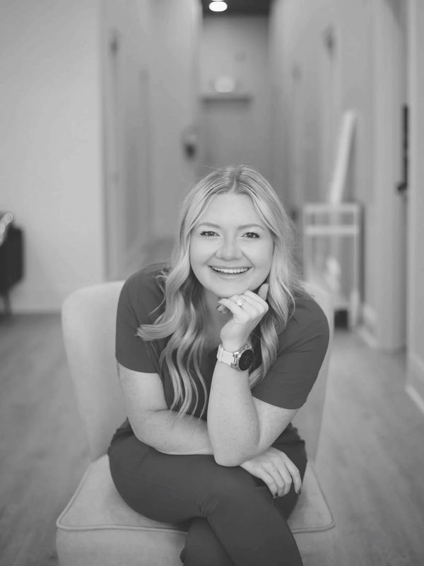 Smiling esthetician at A Hidden Gem Beauty Bar in Mandeville, LA, seated in treatment hallway