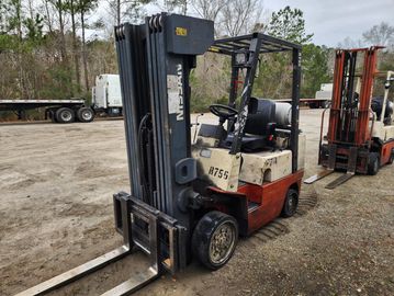 A forklift parked outdoors on a dirt surface near trees.