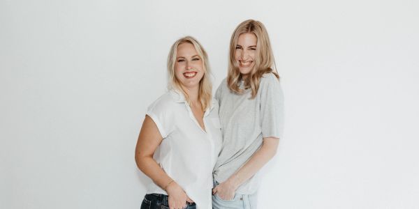 Two smiling women standing against a white background.