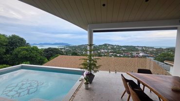 Modern terrace with a pool overlooking a scenic coastal town and hills.