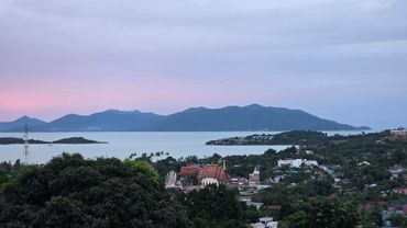 Scenic view of a coastal town with mountains and a temple at sunset.