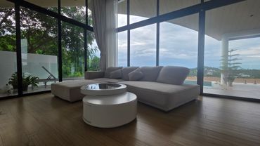 Modern living room with large windows, gray sofa, and round white coffee table overlooking a scenic view.