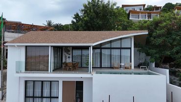 Modern white house with large windows and a pool on the upper floor.