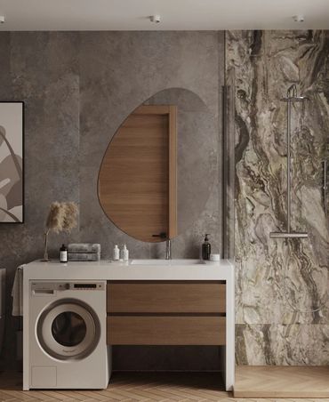 Modern bathroom with washing machine, wooden drawers, and organic-shaped mirror.