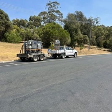 White utility vehicle towing equipment on a trailer parked on a roadside.