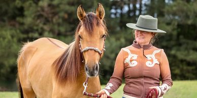 A woman in a hat holding a brown horse by the reins outdoors.
