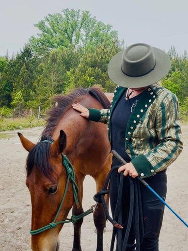 Person in a striped jacket and wide-brimmed hat petting a brown horse.