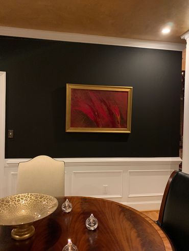 Elegant dining area with dark wall, framed abstract art, and polished wooden table.