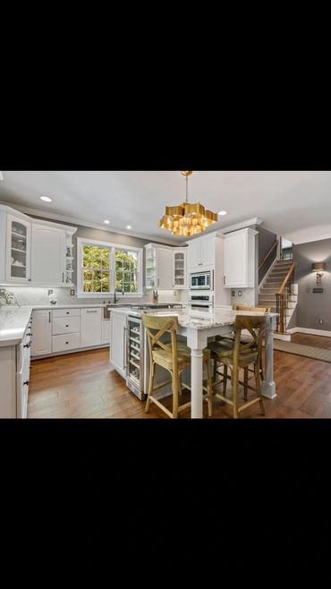 Bright kitchen with white cabinetry and wooden stools around a marble island.