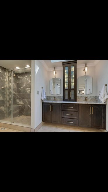 Modern bathroom with dual sinks, dark wood cabinetry, and a glass-enclosed shower with marble tiles.