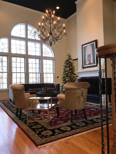 Elegant living room with large windows, chandelier, and decorated Christmas tree.
