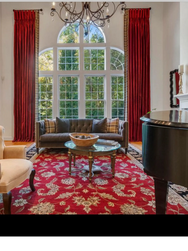 Elegant living room with red curtains, a grand window, and a piano.
