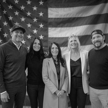 Group of five people standing in front of an American flag.