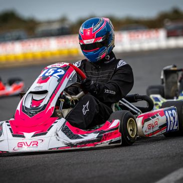 Person racing a pink and white go-kart on a track.
