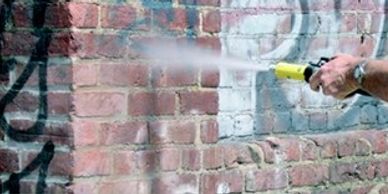 Man removing graffiti from a brick wall