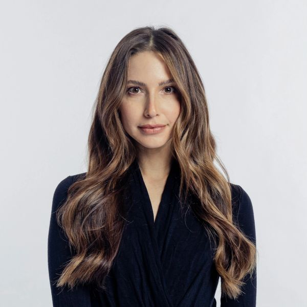 Young woman with long wavy hair wearing a black top against a plain background.
