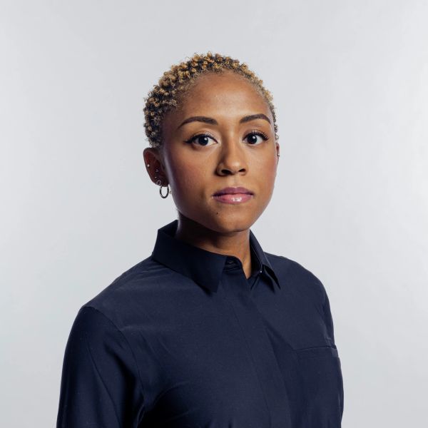 Confident woman with short curly hair wearing a dark shirt against a light background.