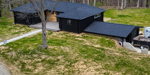 Modern black house with a large tree in the front yard.