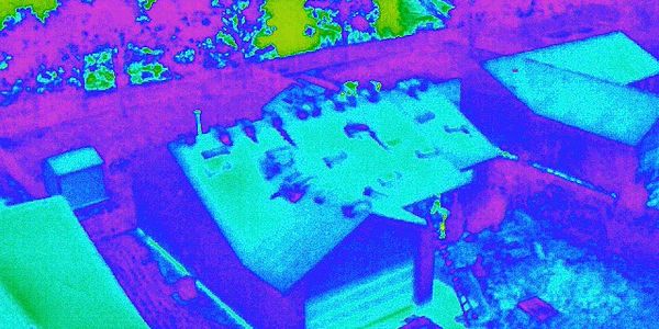 Thermal image of a building and surrounding area with heat signatures.