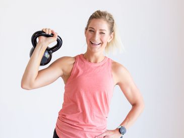 Smiling woman in workout clothes holding a kettlebell with confidence.