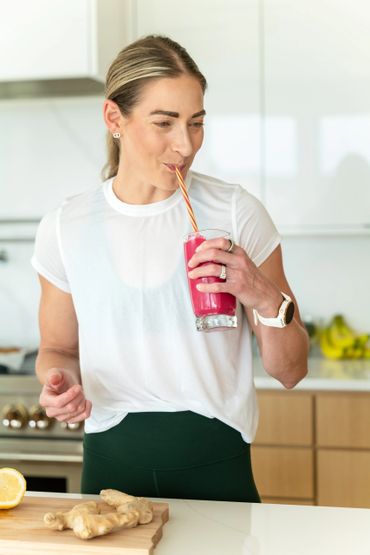 A woman enjoys a vibrant red smoothie in a modern kitchen.