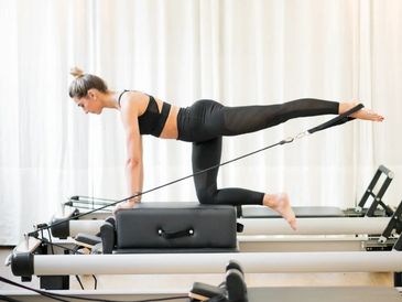 Woman performing Pilates exercise on reformer machine in bright studio.