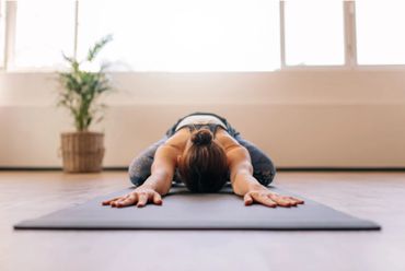 Person practicing yoga child's pose on a mat indoors.
